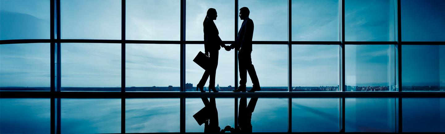 clienti che si presentano dandosi la mano davanti una vetrata in penombra